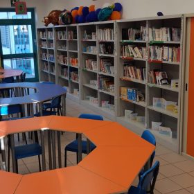 Biblioteca con scaffali di libri e tavoli a forma di trapezio che formano tre tavoloni circolari con sedie