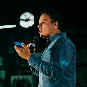 Una persona conduce un discorso al microfono mentre regge un cellulare